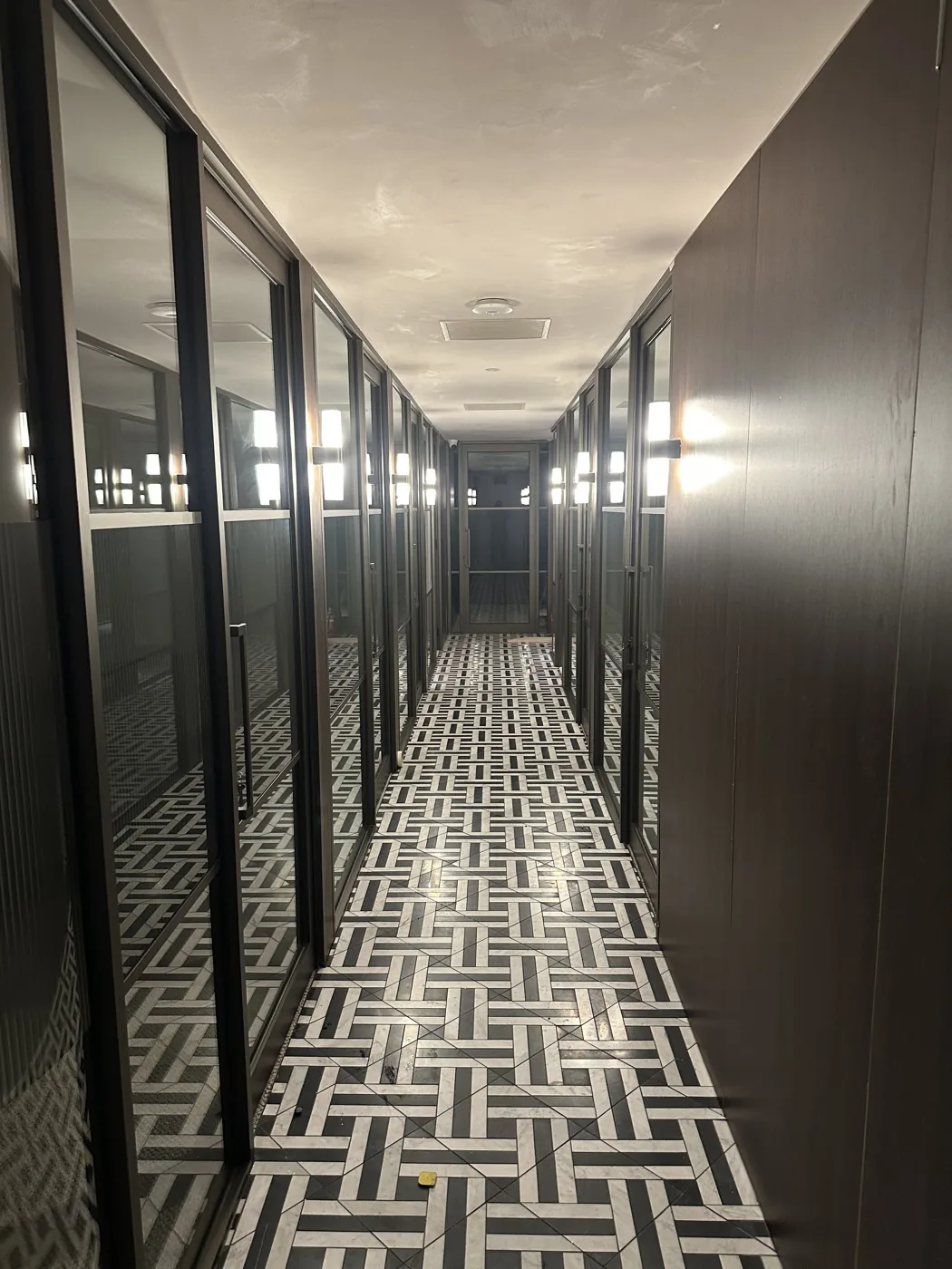 A glass-partitioned office corridor with a patterned tile floor, lit along both sides