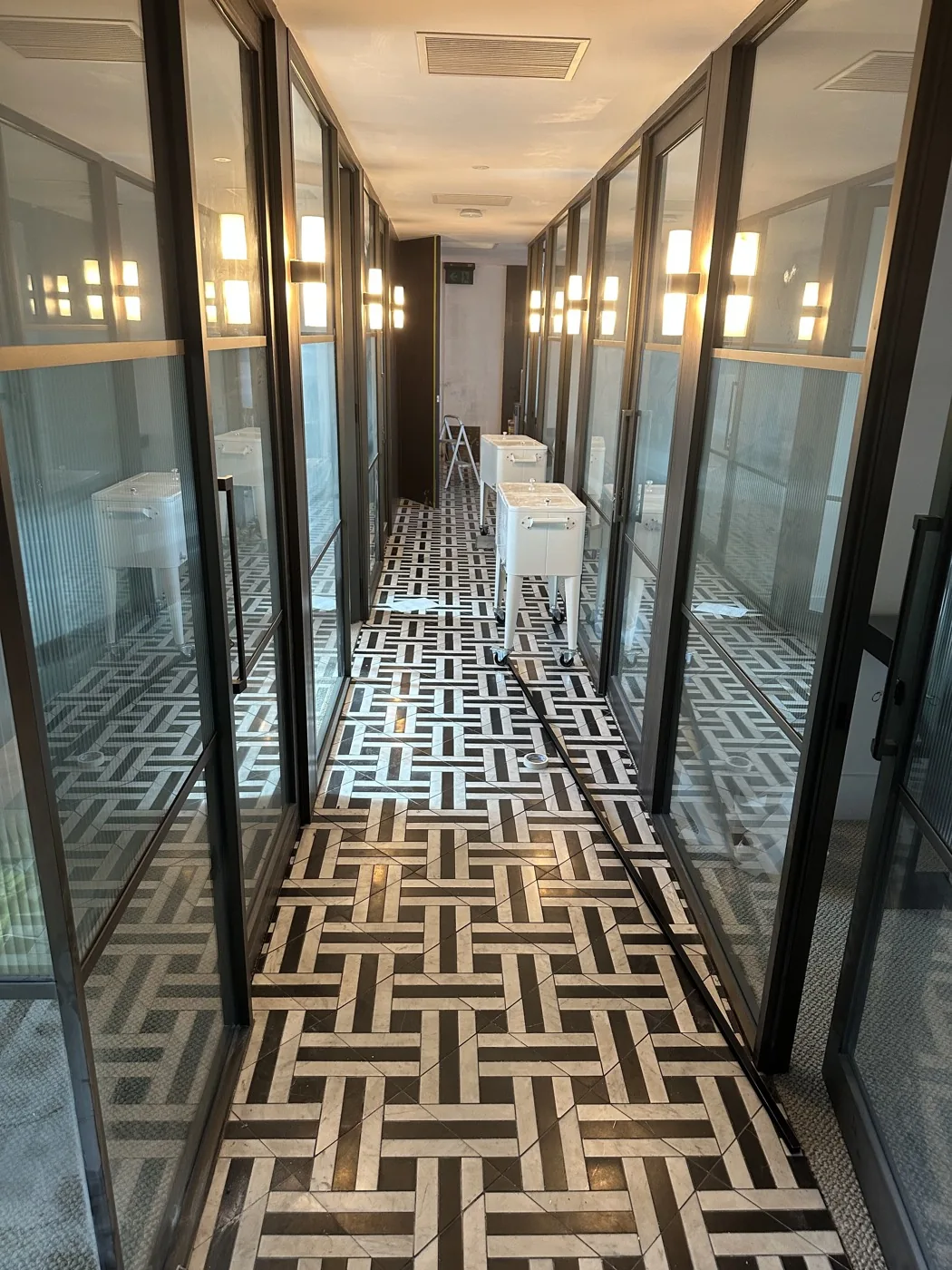 A glass-partitioned office corridor with a patterned tile floor and equipment stacked along one side