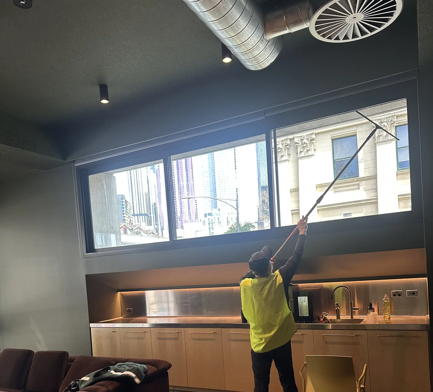 A cleaner using an extension pole on the high windows above an office kitchenette during the clean