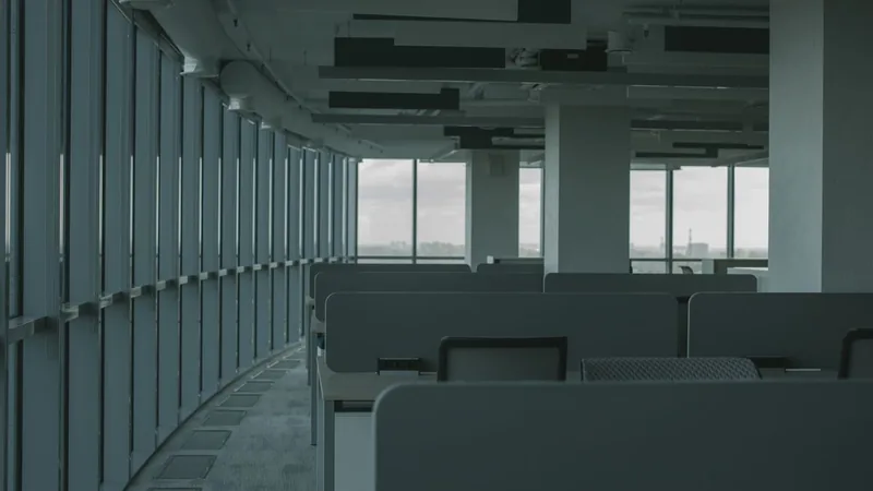 An empty open-plan office with desk pods and a curved wall of windows