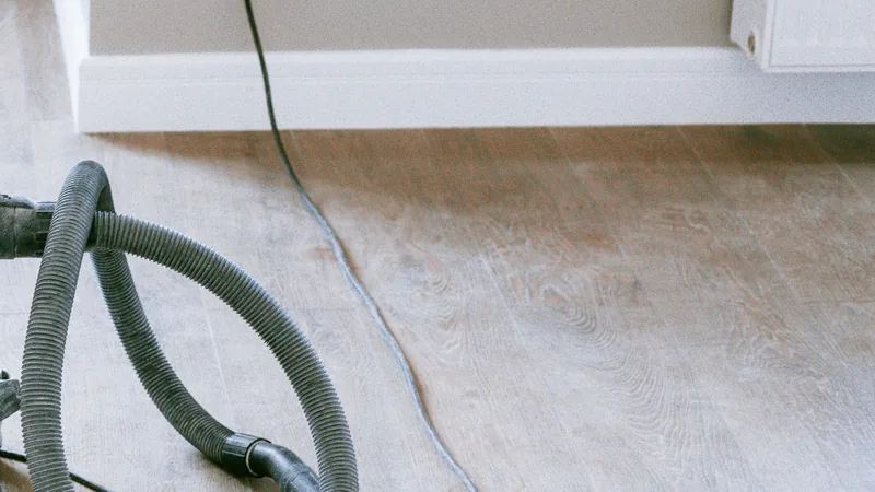 A vacuum cleaner hose and its cable across new timber-look flooring in a freshly renovated interior