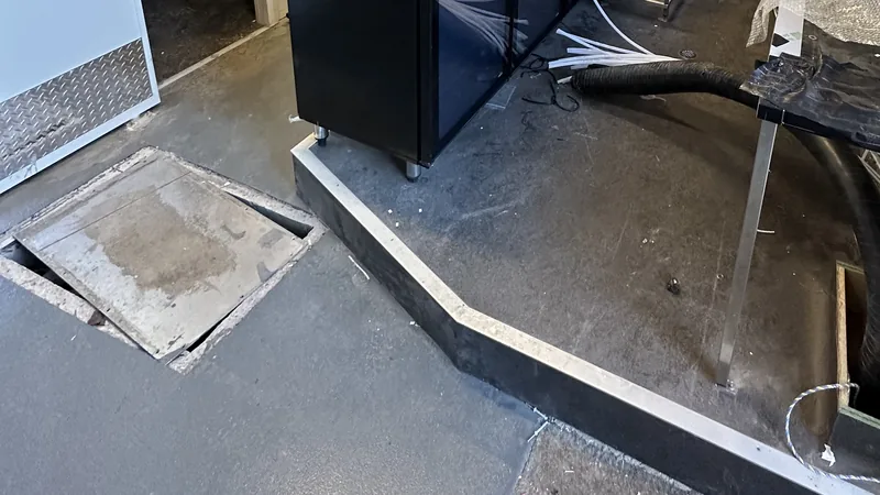 A venue floor during a builders clean, with an open floor hatch, a vacuum hose and a new bar fridge on its plinth