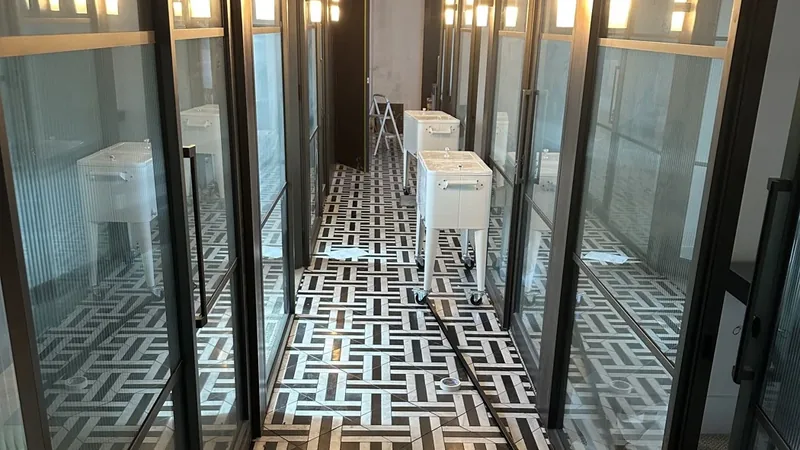A glass-partitioned office corridor with a patterned floor and waste bins left out