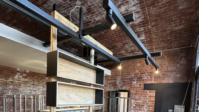 A brick-walled venue mid fit-out, with new open shelving hung from black ceiling beams