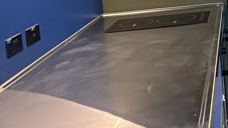 A stainless steel office kitchenette bench with an induction cooktop against a blue wall