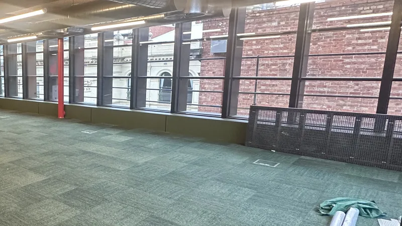 An empty office floor with new carpet tiles and a long wall of windows after a fit-out